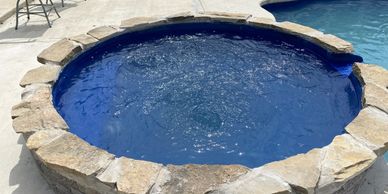 A stone-bordered hot tub bubbling beside a swimming pool.