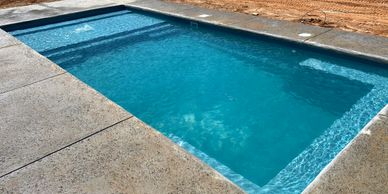 A newly constructed pool with clear blue water and surrounding concrete.