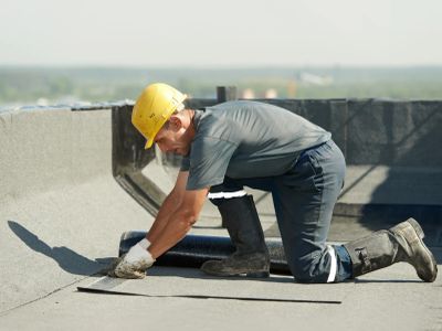 Construction worker laying roofing material on a flat roof.