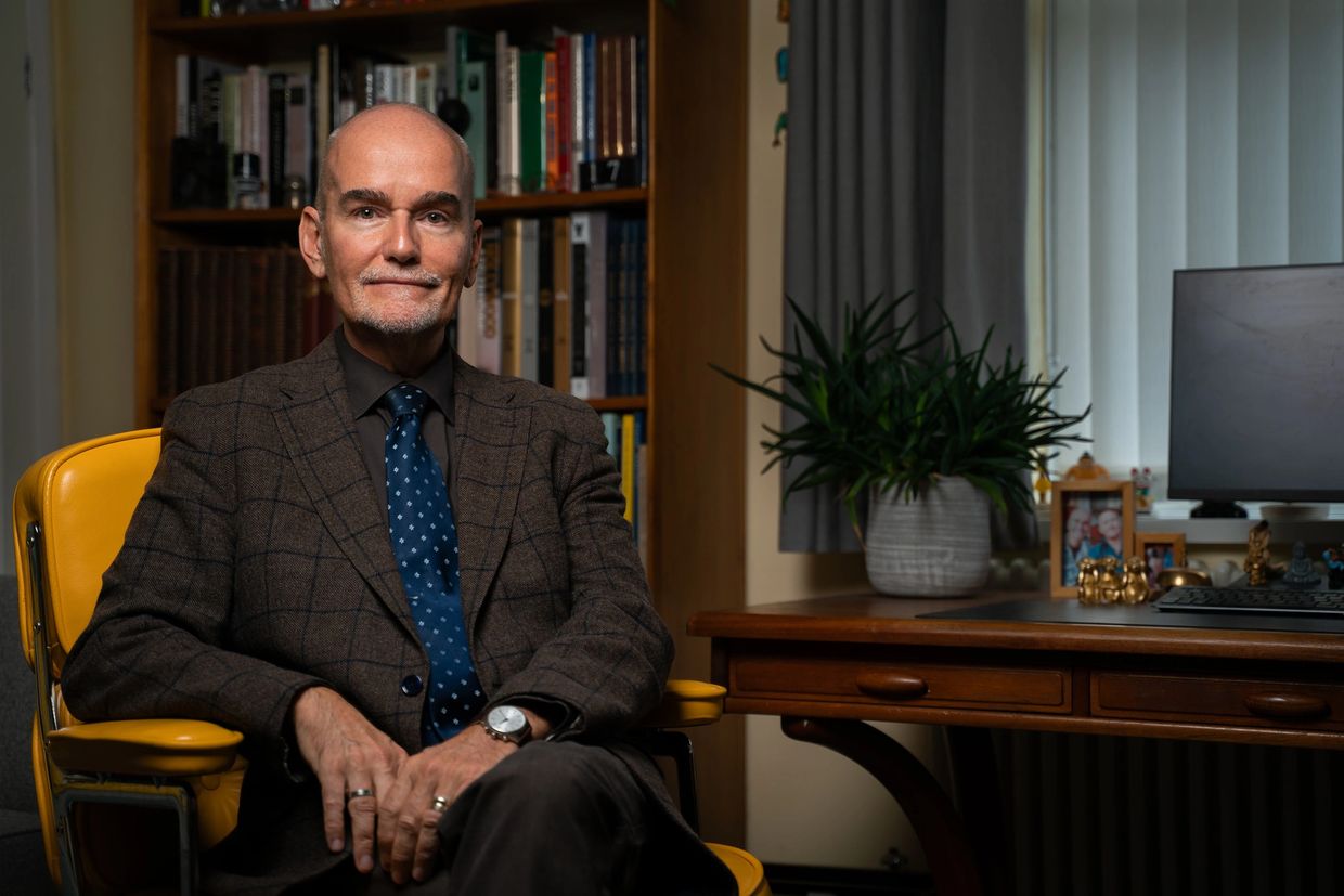 Man in a suit sitting on a yellow chair in an office.