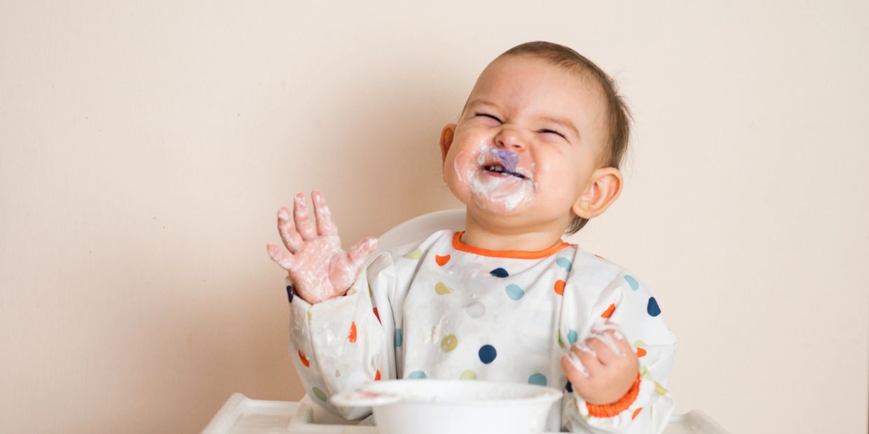 Infant baby happily eating solid food with a spoon