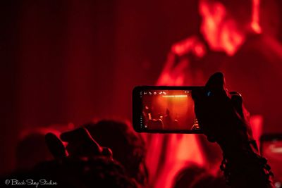Person recording a singer at a red-lit concert.