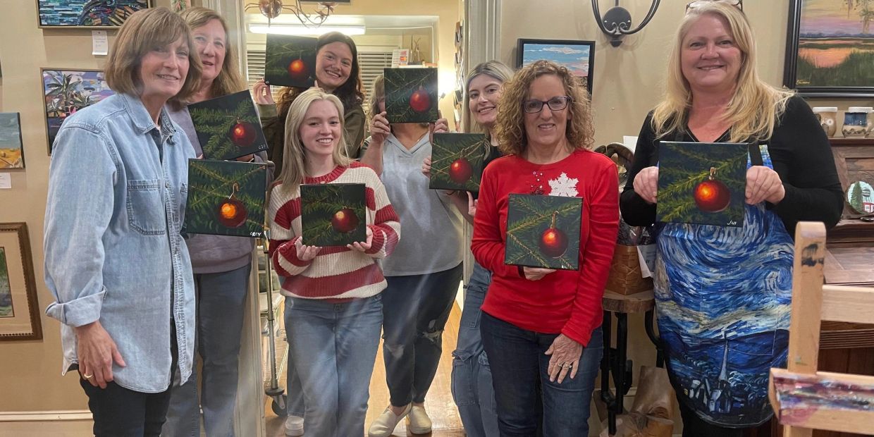 Group of women holding holiday-themed paintings of a red ornament.