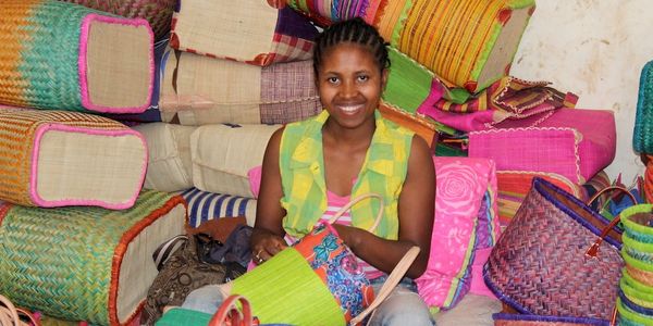 Malagasy artisan posing among colourful bags and baskets.