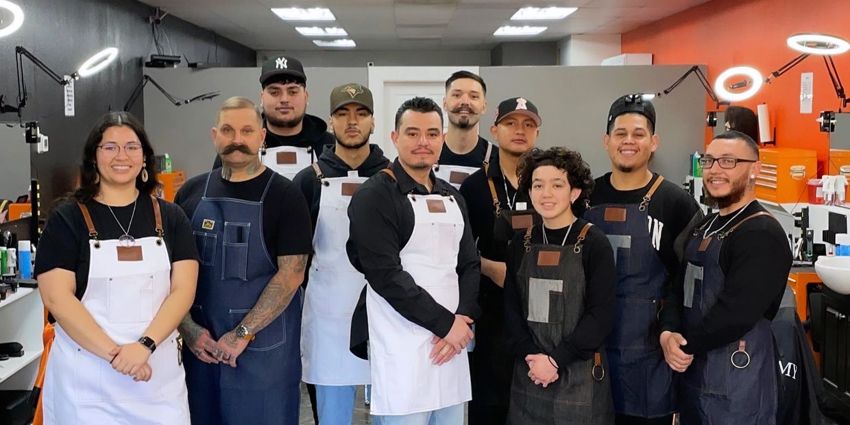 A team of barbers wearing aprons posing in a modern barbershop.