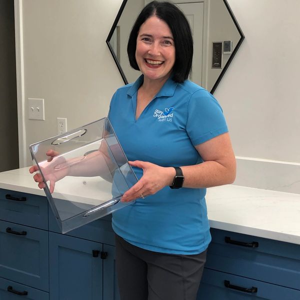 A smiling woman in a blue polo shirt holding a clear container indoors.