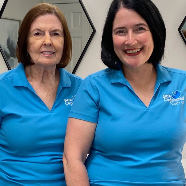 Two women in matching blue polo shirts with logo, smiling indoors.