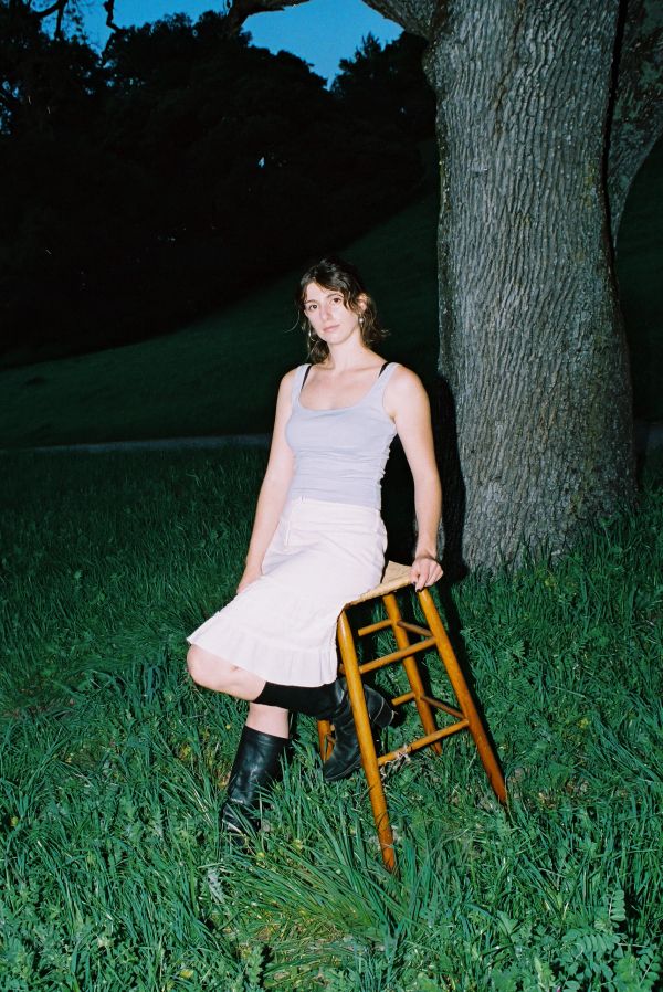 Woman sitting on a wooden stool outdoors at dusk.