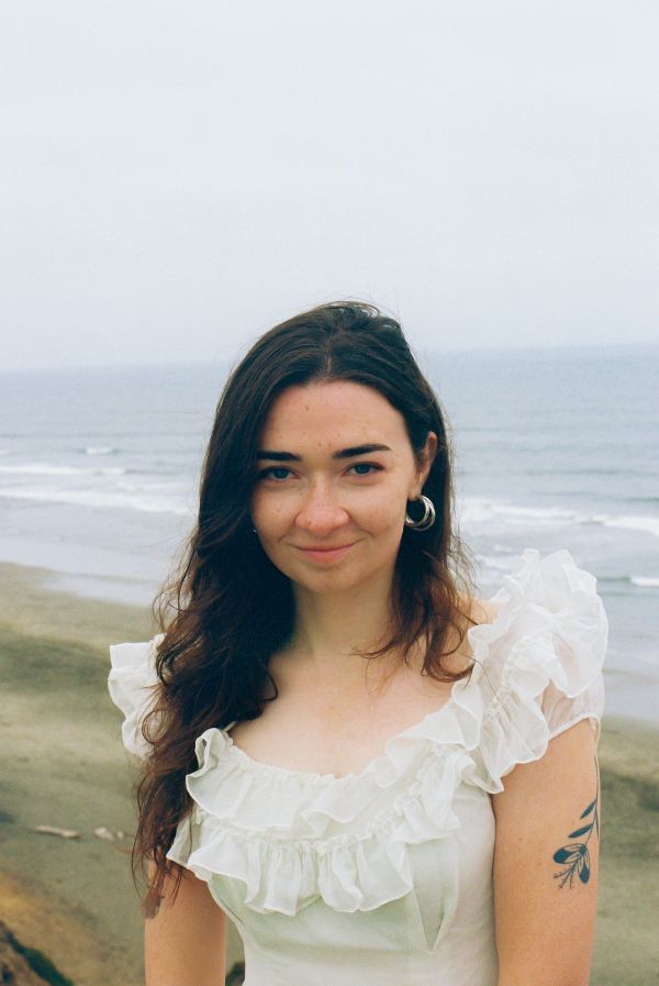 Young woman in a white ruffled dress by the ocean shore.