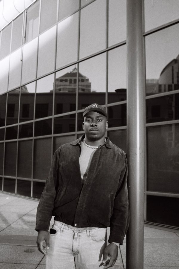 Young man in casual attire stands confidently by a modern glass building.