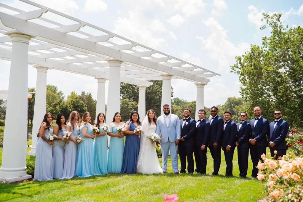 Wedding party posing outdoors under white pergola on sunny day.