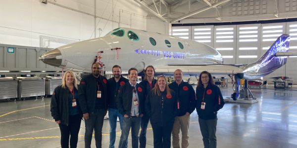 Crew posing in front of a sleek white aircraft inside a hangar.
