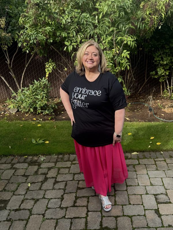 Woman smiling outdoors wearing a black t-shirt and pink skirt.
