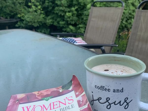Coffee mug with the text "coffee and Jesus" and a Women's Bible on a glass table outdoors.