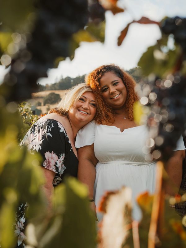 Two women smiling together in a vineyard.