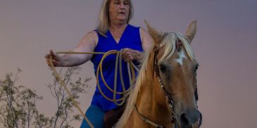 Woman in blue vest holding rope on horse.