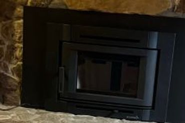 A modern black fireplace insert set in a rustic stone surround with a brick hearth