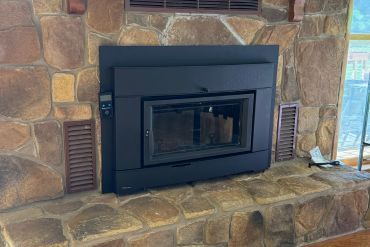 A sleek black fireplace insert installed within a rustic stone surround and brick hearth