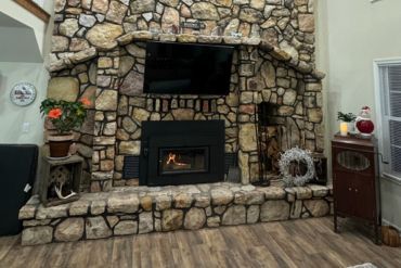A stone fireplace with a wood-burning insert, brick hearth, and mounted TV above, flanked by decor