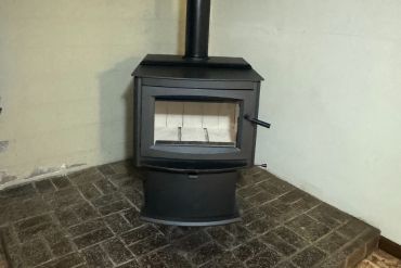 A rustic stone fireplace with a wood-burning insert, brick hearth, TV above, and decorative items