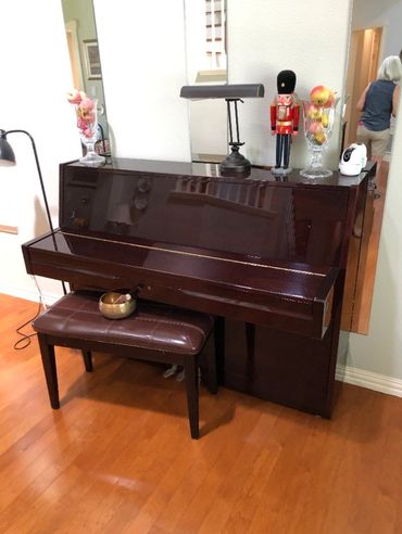 Shiny upright piano with bench and decorative items on top.