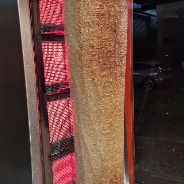 Vertical meat roasting on a rotating spit near heating elements.