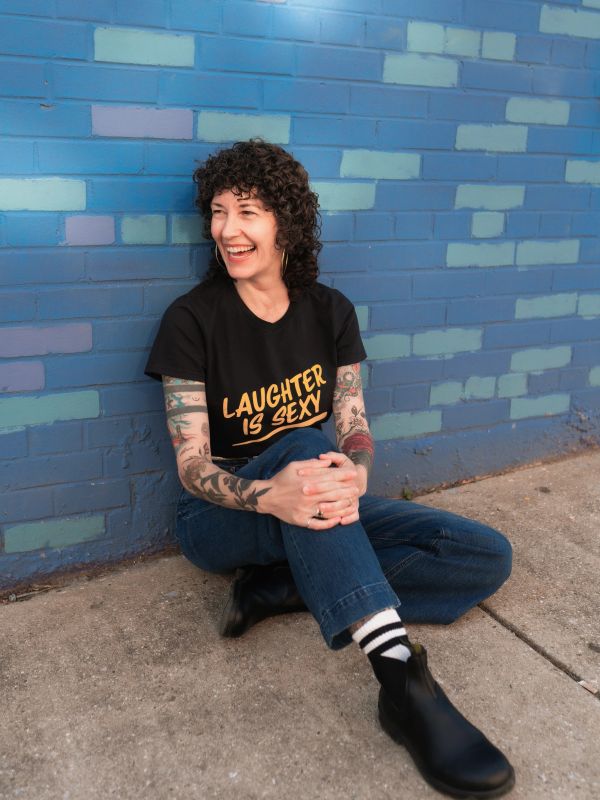 Woman sitting against blue brick wall smiling.
