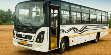 White Tata bus with black and blue stripes parked on a gravel surface.