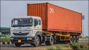 White Tata truck carrying a large orange shipping container on highway.