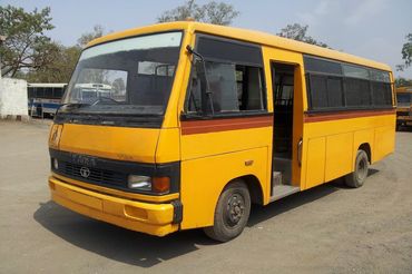 Yellow Tata school bus parked with door open on a sunny day.