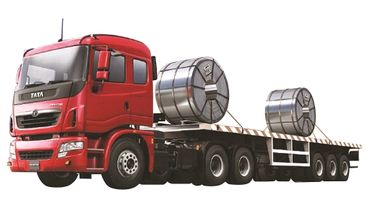 Red Tata truck carrying large steel coils on a flatbed trailer.