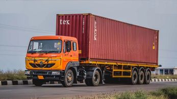Orange truck carrying a large red shipping container on a highway.