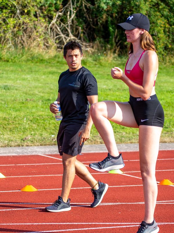 Athlete warming up with coach on a track field.