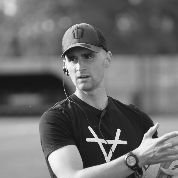 Man in a cap speaking with hand gesture, wearing a watch and earphones.
