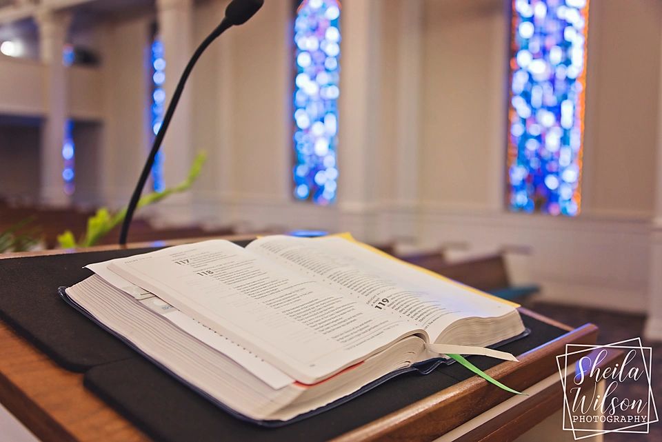 Open Bible on church podium with stained glass windows.