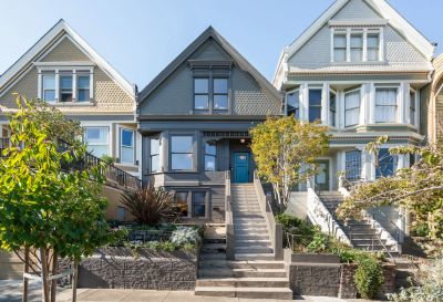 Three colorful Victorian houses with stairs and greenery.