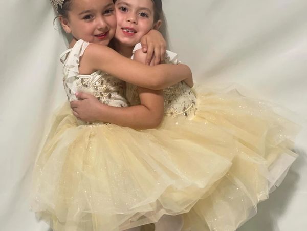 Two young girls in matching yellow ballerina dresses hugging each other.
