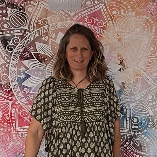 Woman smiling in front of a colorful mandala tapestry.