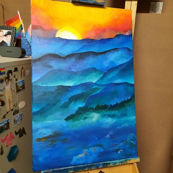A vibrant painting of blue mountains under a bright orange and yellow sunset.
