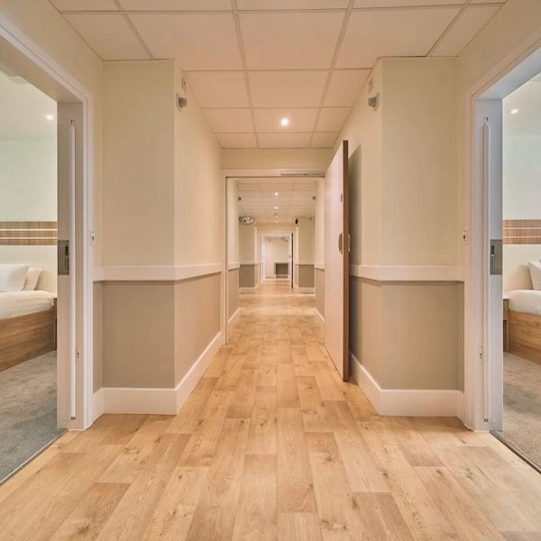 Hotel hallway with wooden floors and open doors to bedrooms.