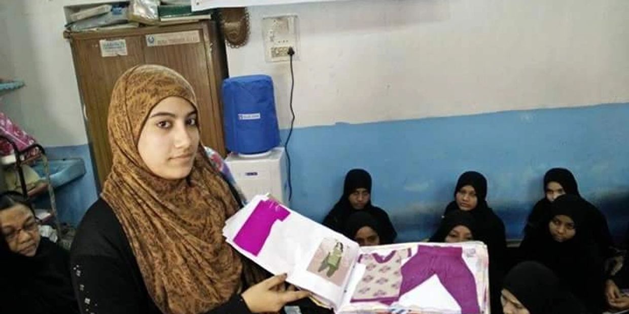 Young woman in hijab presenting handmade clothing designs in a community room