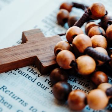 A rosary and cross sit on top of scripture text.