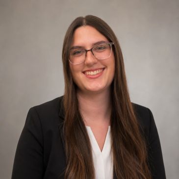 Smiling woman with long hair, glasses, and a black blazer.