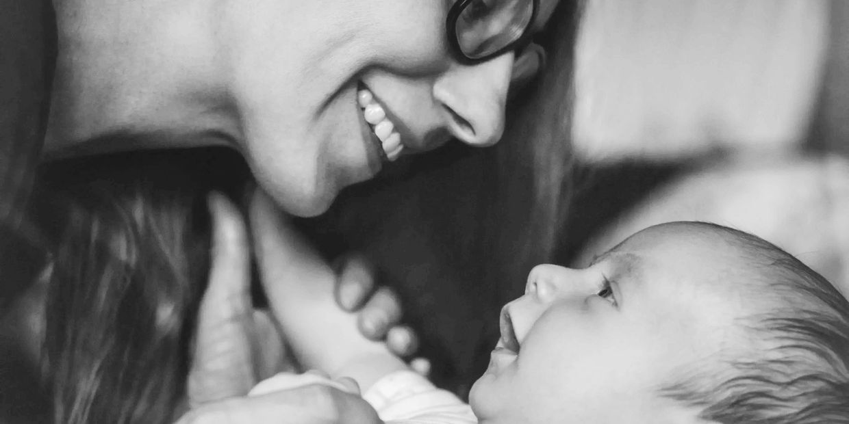 A smiling woman lovingly gazes at a baby in her arms.