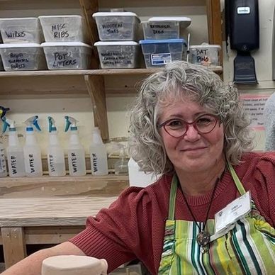 Smiling woman with curly gray hair in an apron at a workshop.