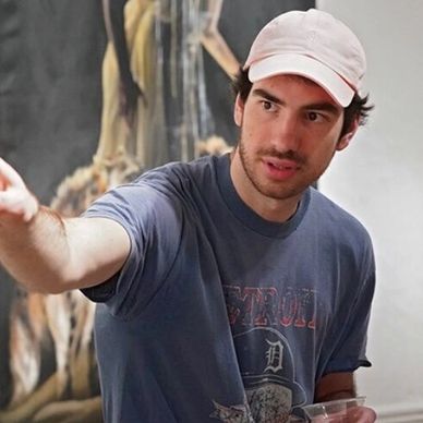 Man wearing a white cap and dark t-shirt gesturing with his hand.