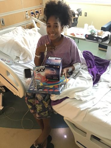Smiling girl in hospital holding board games and a gift.