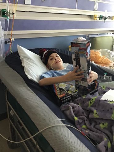 Child in hospital bed holding toys and smiling.