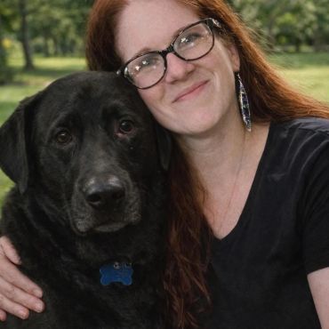 Woman with red hair hugging a large black dog.