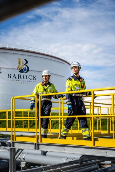 Two workers in safety gear walk on industrial platform at Barock facility.
